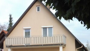 Un edificio residencial de dos plantas con un balcón, una puerta principal y una escalera que lleva a la entrada.
