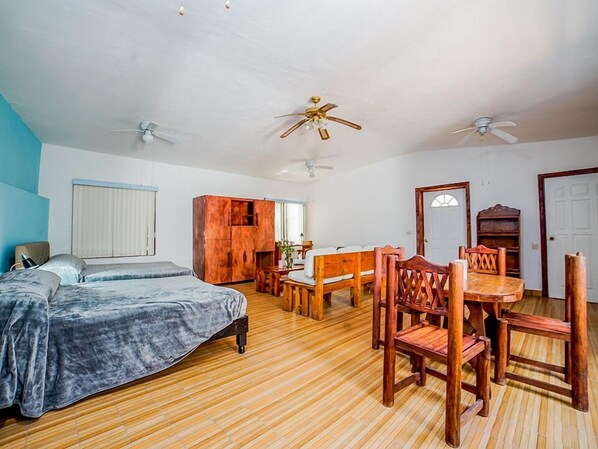 A bedroom with a bed, a wooden wardrobe, a desk with a chair, and two ceiling fans.