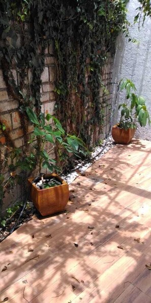 A brick wall with dense ivy growth, two large potted plants, and a wooden floor with scattered leaves.