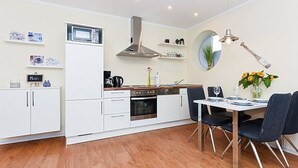 Et moderne køkken med hvide skabe, en indbygget ovn og et spiseområde med et bord og stole.