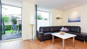 En moderne stue med en sort lædersofa, et hvidt sofabord og en glasdør, der fører ud til et udendørs område.