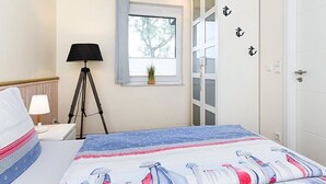 Et soveværelse med seng, skrivebord, lampe, vindue og garderobeskab.
