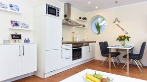 Et moderne køkken med hvide skabe, en mikrobølgeovn og et spiseområde med bord og stole.