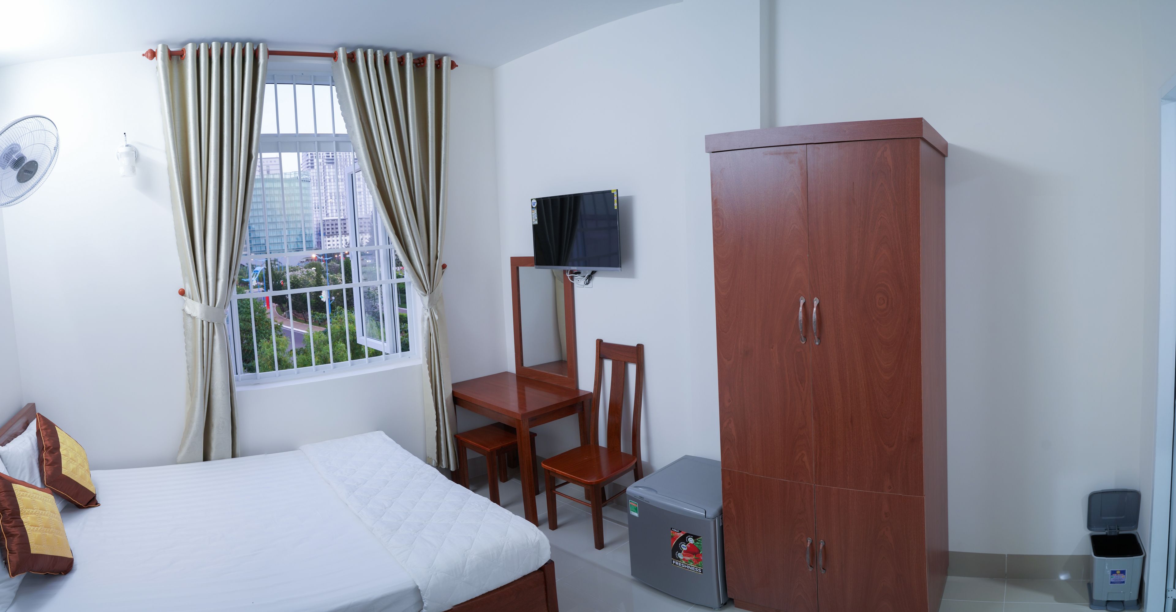 Une chambre à coucher comprenant un lit, un bureau, une chaise, une armoire, un téléviseur et une fenêtre avec des rideaux.