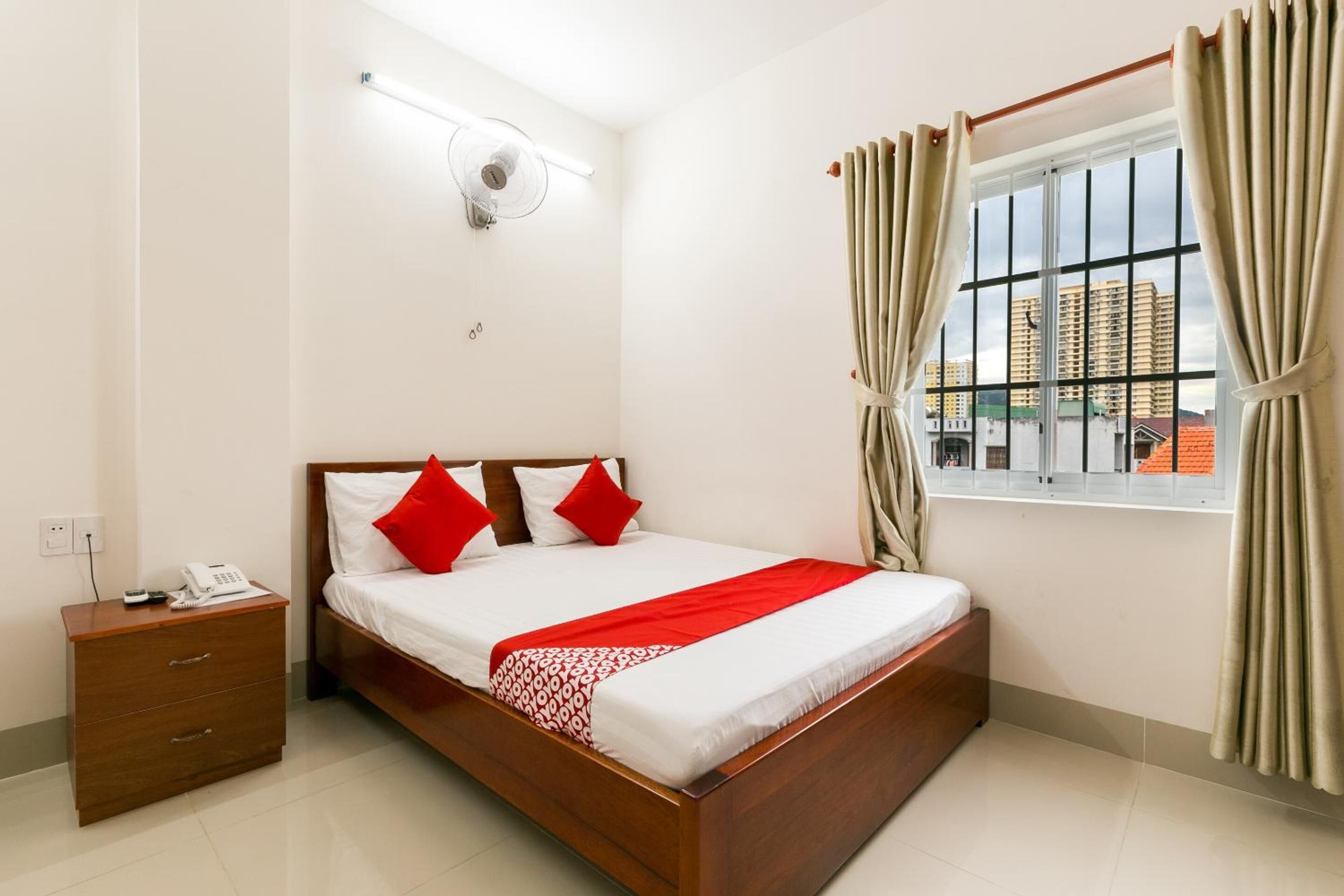 A neatly arranged bedroom with a wooden bed, a bedside table with a phone, and a window with curtains.