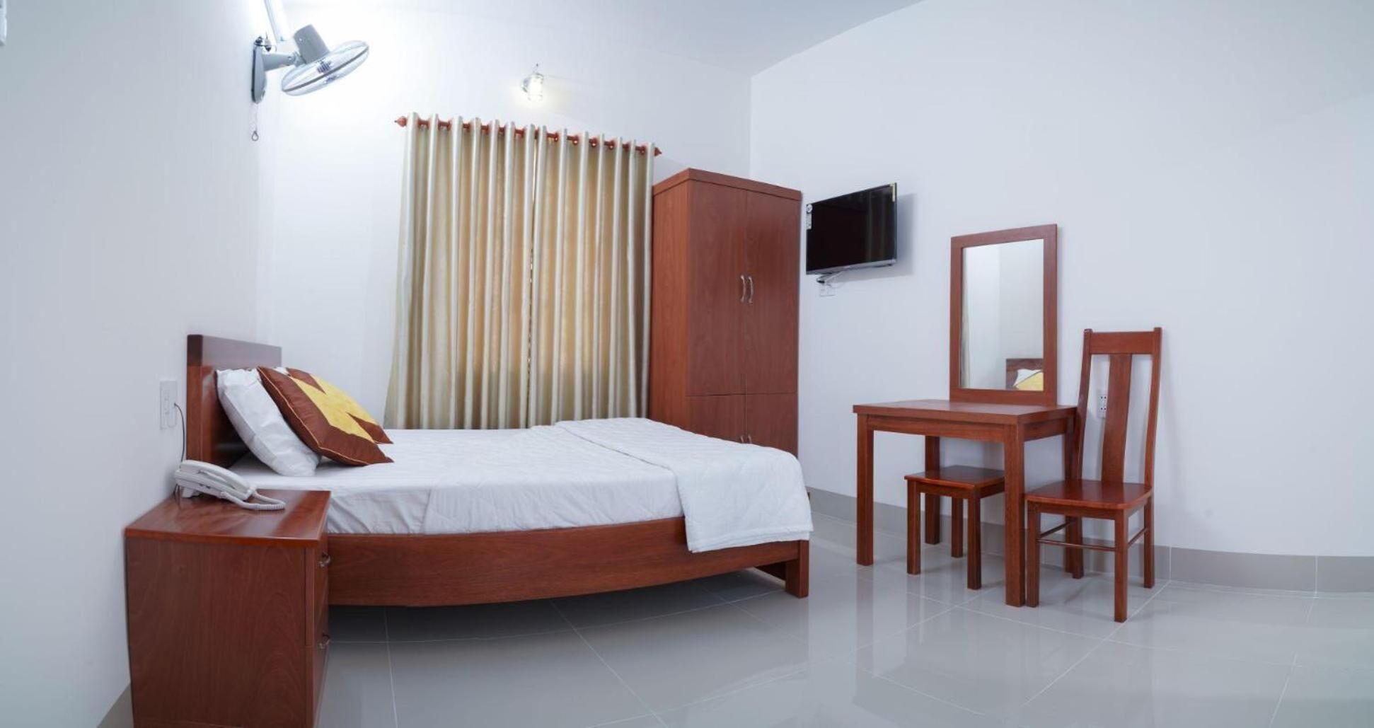 Une chambre à coucher comprenant un lit, une armoire en bois, un bureau avec une chaise, une télévision et un miroir.