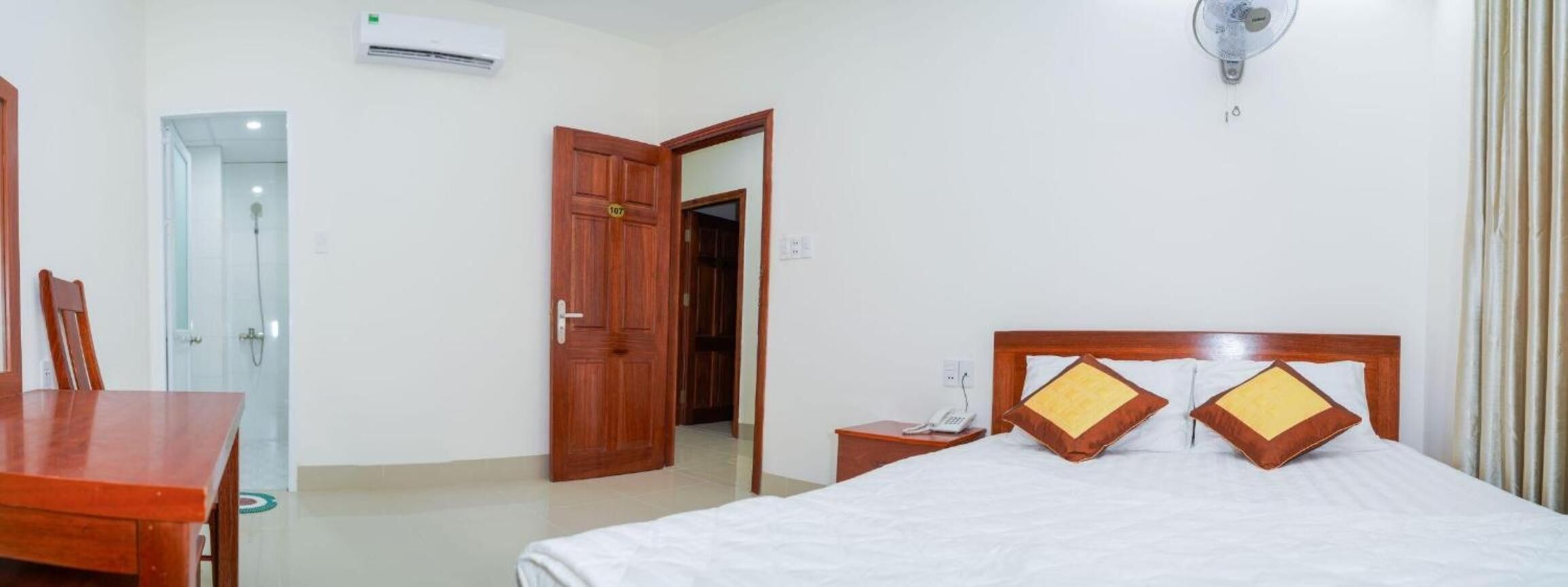 Une chambre d’hôtel avec un lit, une table de chevet en bois, un bureau et une porte ouverte donnant sur une autre pièce.