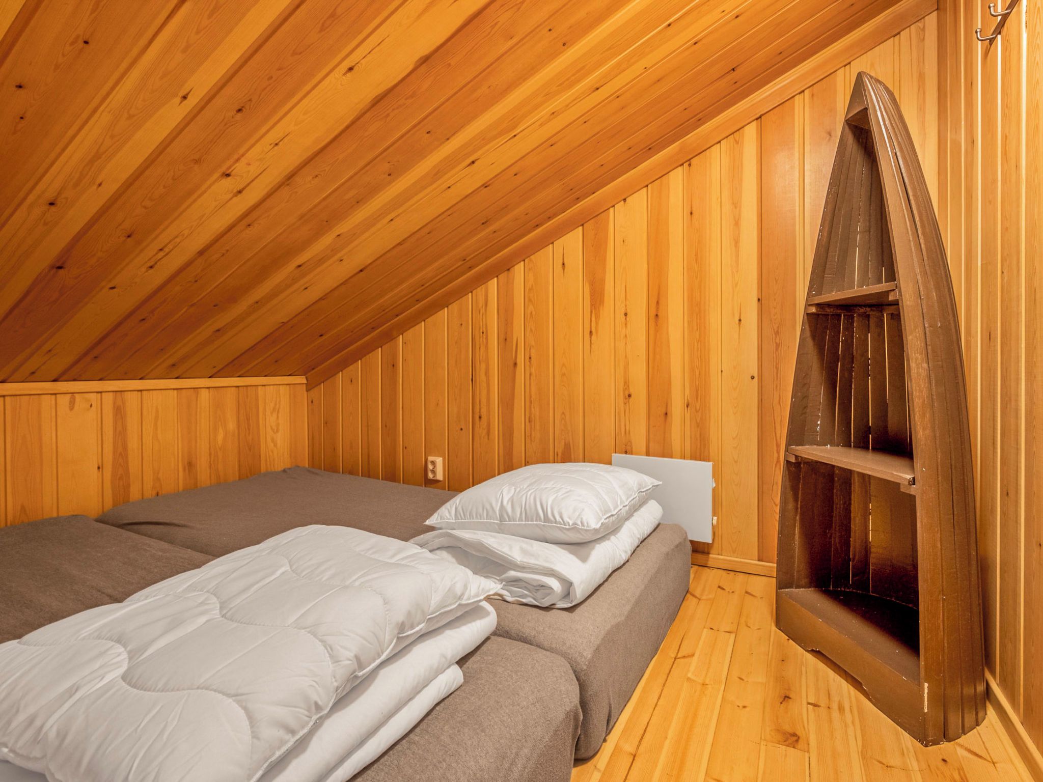 A room with wooden walls and a sloped ceiling. There are two beds with white bedding and a wooden bench against the wall.