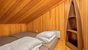 A room with wooden walls and a sloped ceiling. There are two beds with white bedding and a wooden bench against the wall.