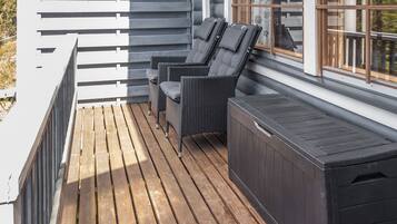 A wooden deck with two wicker chairs and a built-in bench.