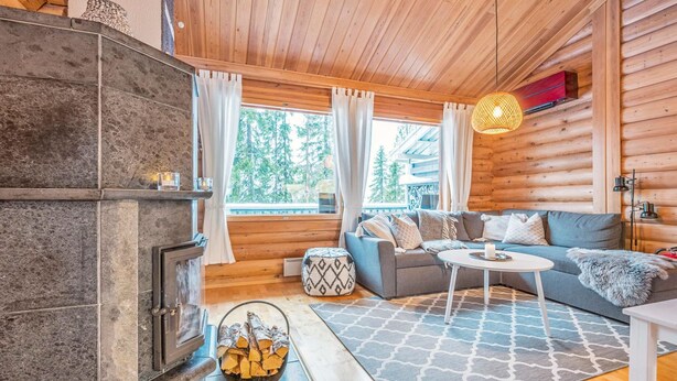 A cozy log cabin interior with a stone fireplace, a sofa set, and a large window offering a view of trees. - Vacation home Aino by Interhome (Kuusamo)