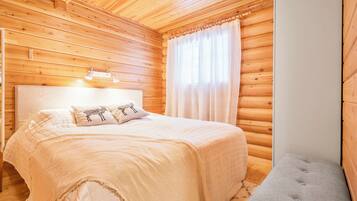 Ein Schlafzimmer einer Holzhütte mit einem Bett, Kissen, einer Nachttischlampe, einem Fenster mit Vorhängen und einer kleinen Bank.
