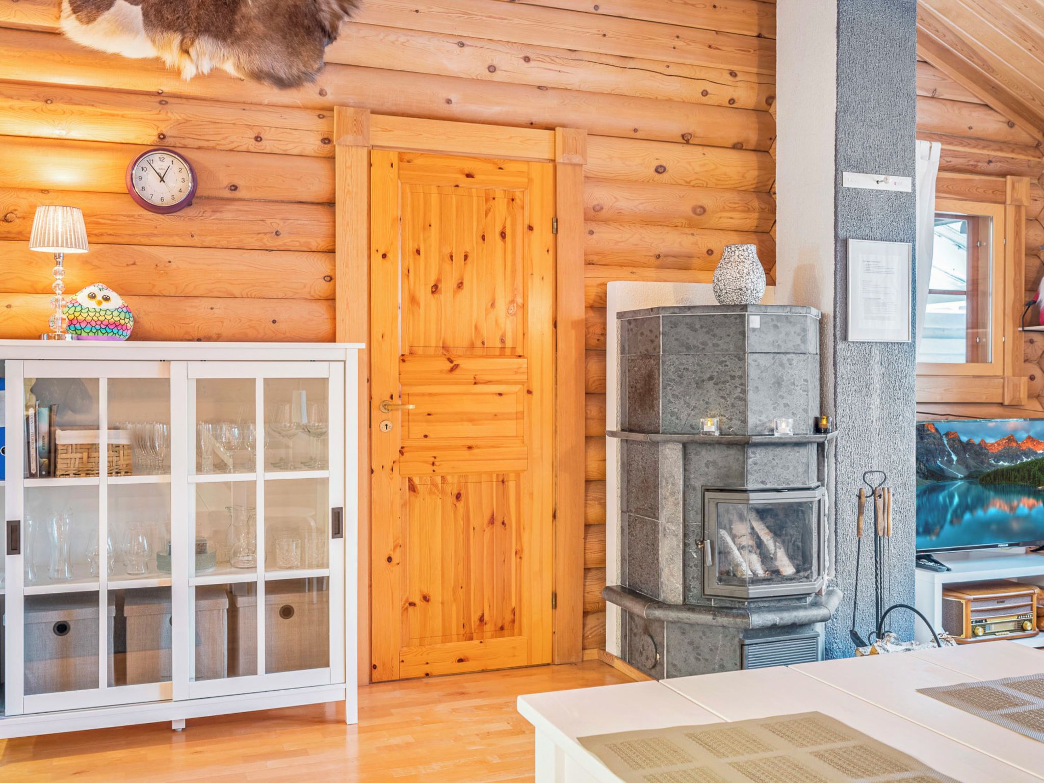 A wooden interior with a wooden door, a cabinet with glass doors, a stone fireplace, and a television on a stand.