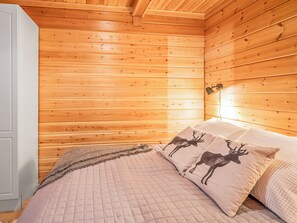 Ein Schlafzimmer mit Holzwandverkleidung, einem Bett mit gesteppter Bettdecke und zwei Kissen mit Hirschmotiven.