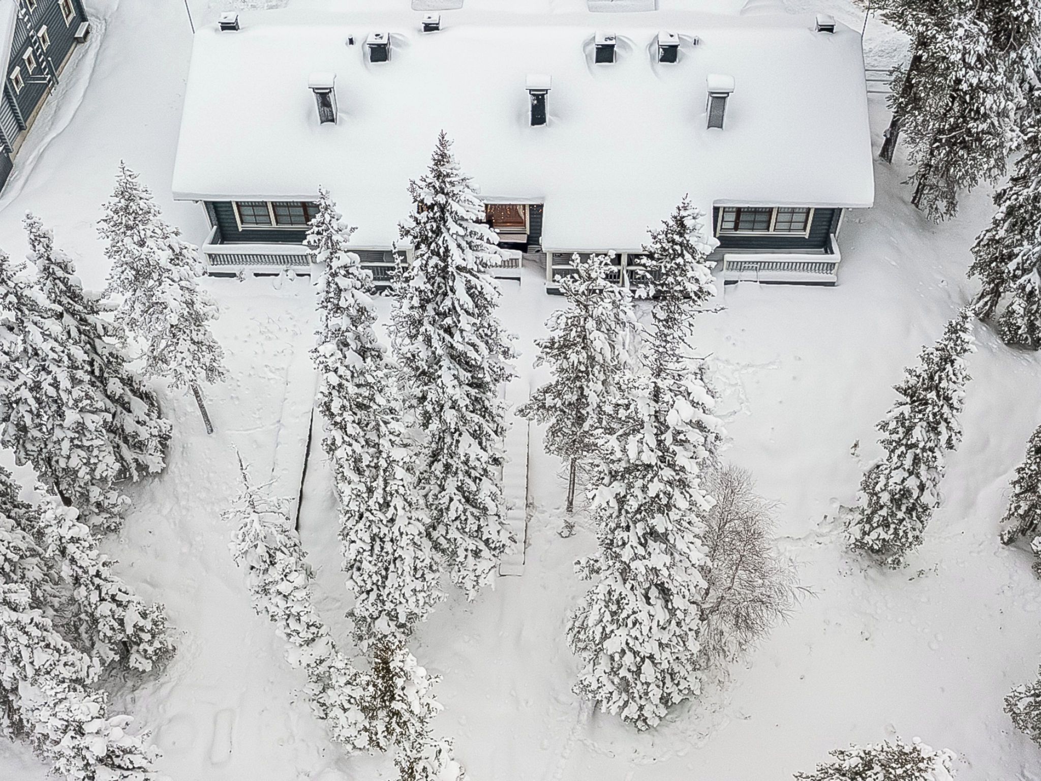 Ein mit Schnee bedecktes Wohnhaus mit mehreren Schornsteinen, umgeben von schneebedeckten Bäumen.