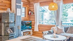 A cozy cabin interior with a stone fireplace, wooden walls, a television, and a sofa with cushions. - Vacation home Aino by Interhome (Kuusamo)