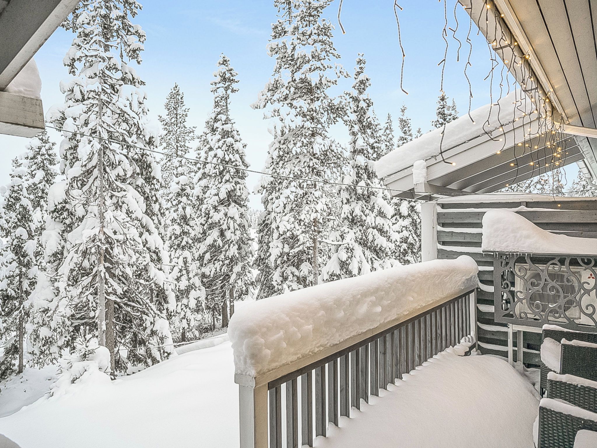A snow-covered balcony with a railing, overlooking a forest of snow-laden trees.