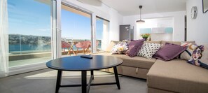 Una sala de estar moderna con un sofá, una mesa redonda y vista al mar a través de amplios ventanales.