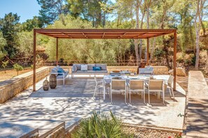 Une terrasse extérieure dotée d’une pergola en bois, de meubles blancs et d’un mur en pierre.