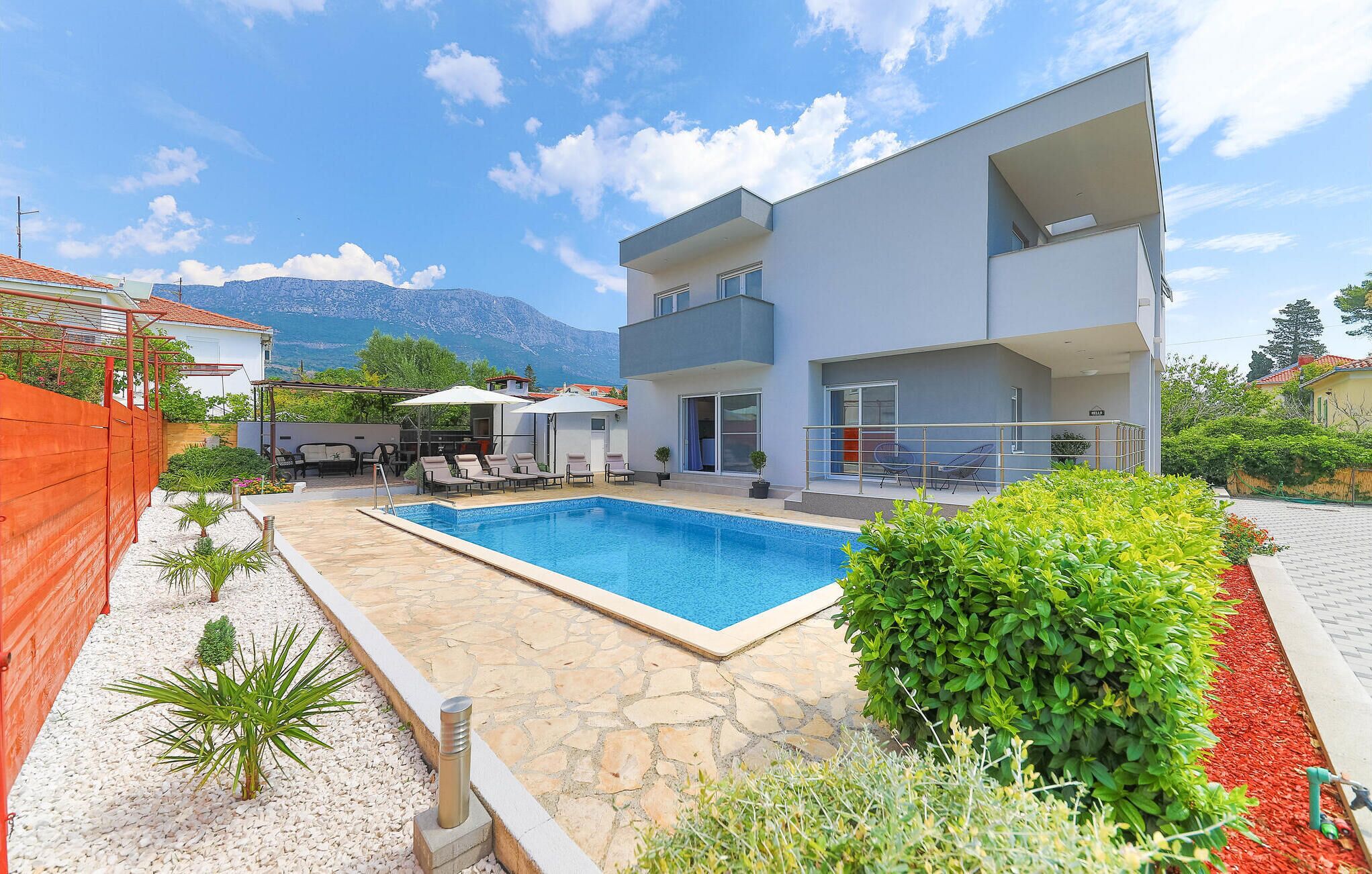 A modern two-story house with a swimming pool, outdoor furniture, and a mountain view.