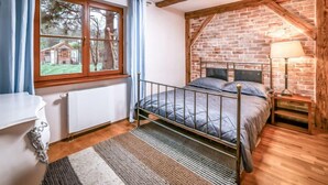 Een slaapkamer met een metalen bedframe, een bakstenen muur, een raam met gordijnen en een houten vloer.
