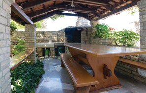 Enjoy dining or socializing around the large table with benches in this serene outdoor space surrounded by lush greenery.