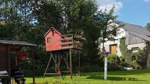 A garden with a pond, a wooden swing set, and a red playhouse.