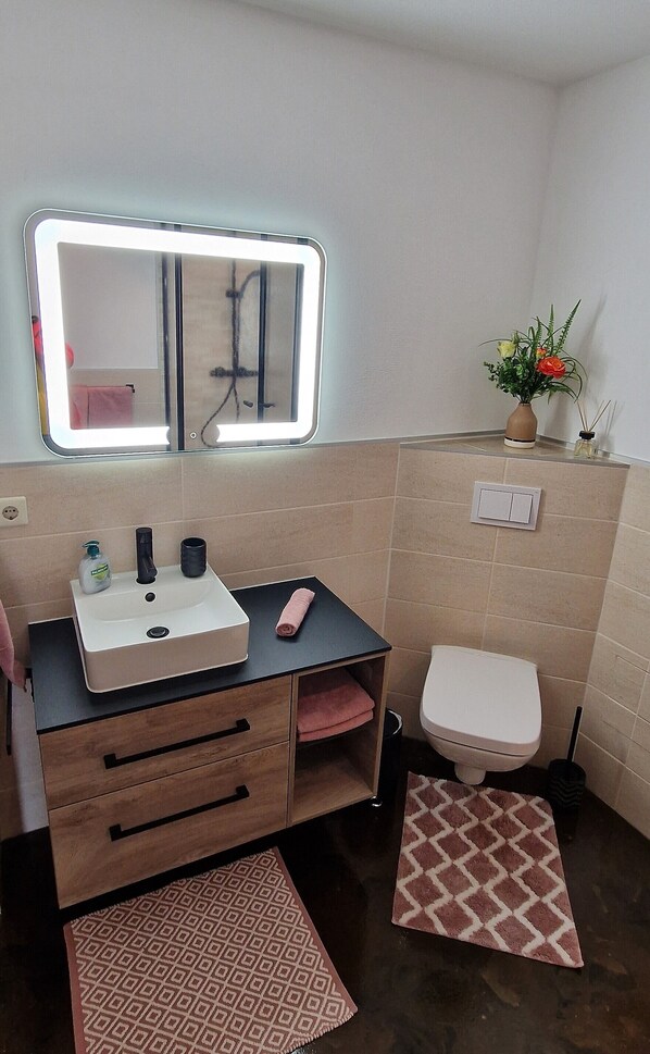 A bathroom with a sink, mirror, toilet, and a small potted plant.
