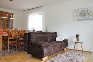 En stue med en brun lædersofa, et træspisebord, stole og et sofabord i glas med en vase.