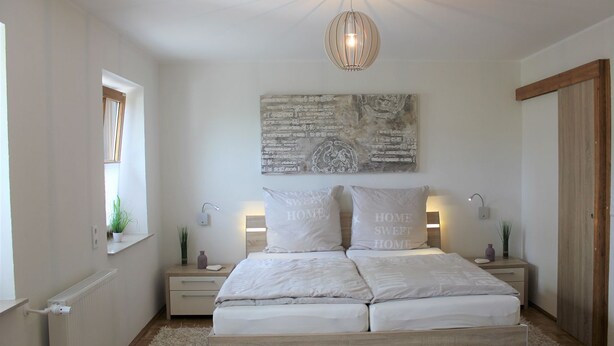 A bedroom with a wooden bed, bedside lamps, a ceiling light, a window, and a wall art piece. - Vacation apartment in dream location, 92m², terrace, garden, top equipment (Halver)