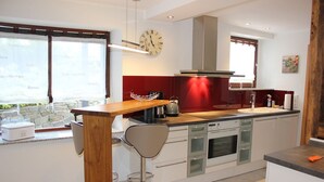 A modern kitchen with a wooden bar counter, a stainless steel kettle, and a clock on the wall. - Vacation apartment in dream location, 92m², terrace, garden, top equipment (Halver)