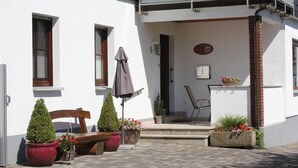 A building with a white exterior, a wooden bench, potted plants, and a small outdoor seating area. - Vacation apartment in dream location, 92m², terrace, garden, top equipment (Halver)