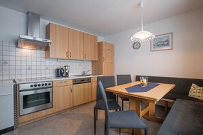 Una cocina compacta con estufa, horno y lavavajillas, una mesa de comedor con sillas y un sofá.