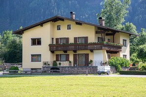 A two-story building with a balcony, a stone wall, and a vehicle parked in front.
