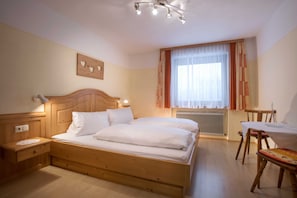 A bedroom with a wooden bed, bedside table, and a small table with chairs. - Vacation apartment in the country house - Ferienhof Stadlpoint (Ried im Zillertal)
