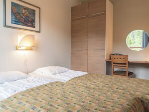 Une chambre à coucher comprenant un lit, une armoire, un bureau avec une chaise, une lampe fixée au mur et un tableau encadré.