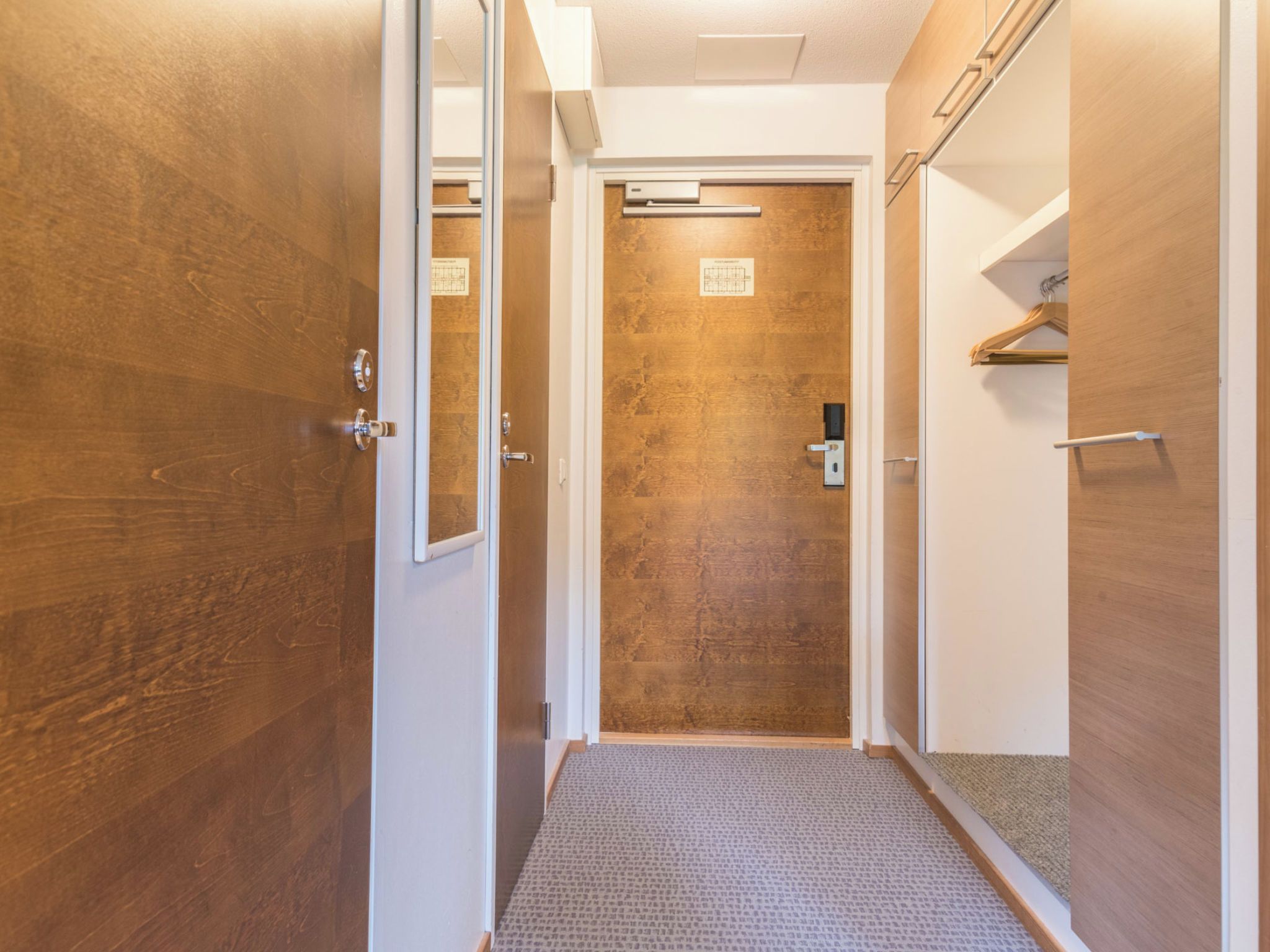 A hallway with wooden doors, a carpeted floor, and a door with a grid pattern.