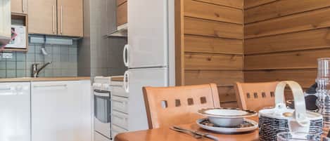 A modern kitchen with white appliances, wooden cabinets, and a dining table set with cutlery and a teapot.