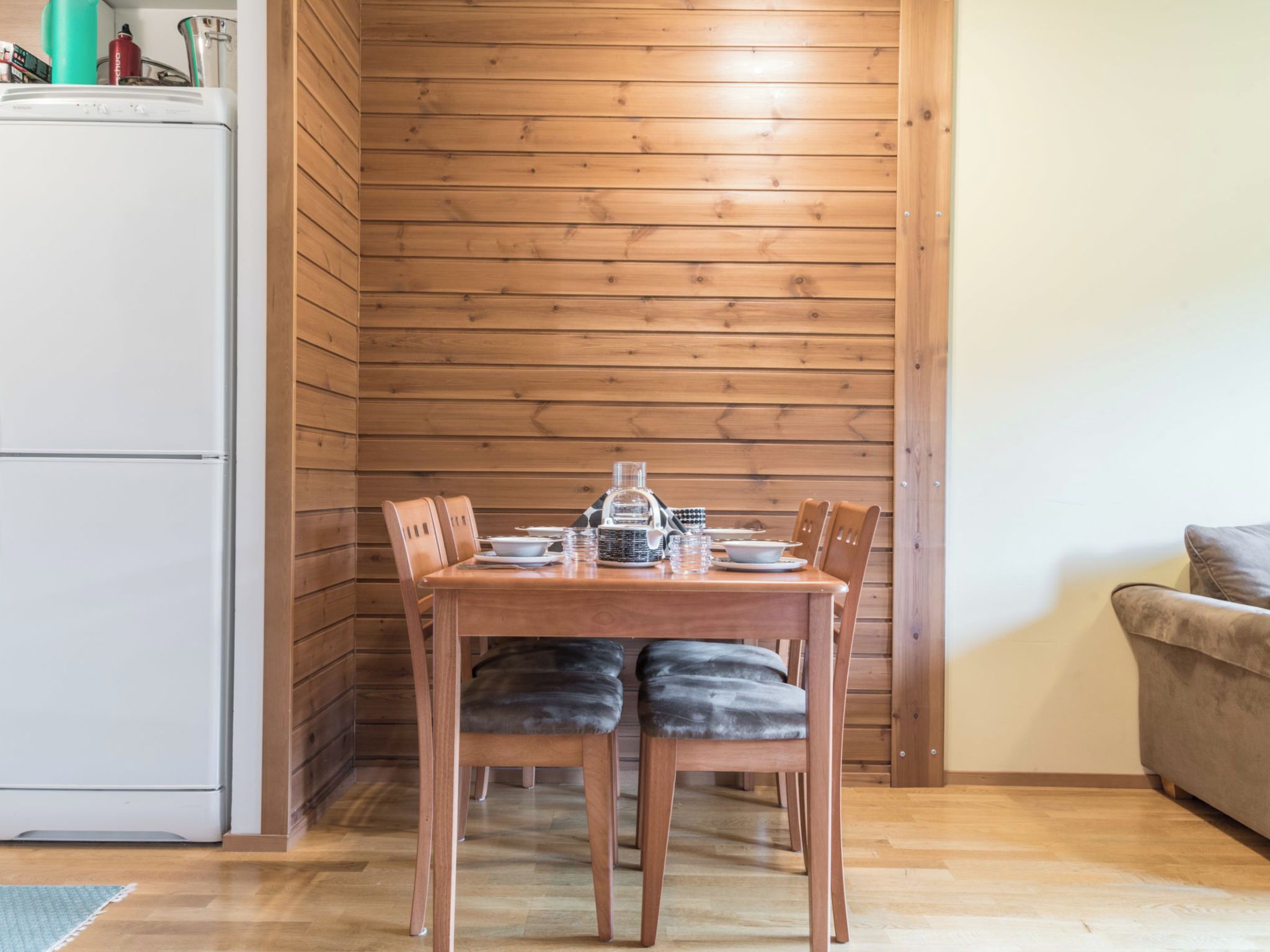 A wooden-paneled room with a dining table set for two, a sofa, and a white refrigerator.