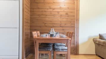 A wooden-paneled room with a dining table set for two, a sofa, and a white refrigerator.