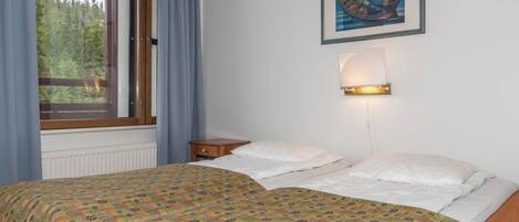 Une chambre à coucher avec un lit, une fenêtre avec des rideaux, une table de chevet, une lampe fixée au mur et un tableau encadré.