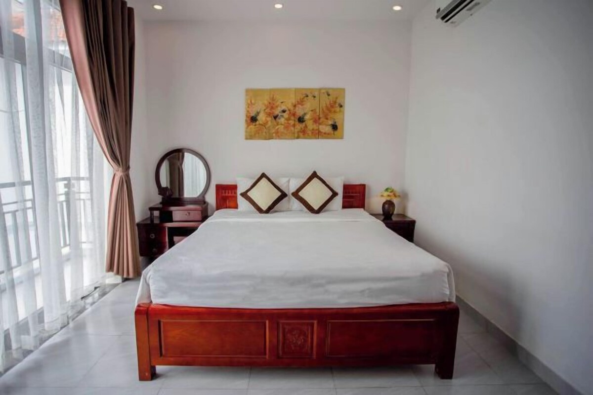 A bedroom with a large bed, a bedside table, a mirror, and a wall-mounted artwork.