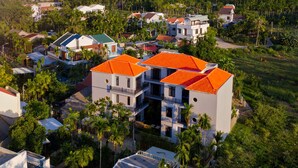 An aerial view of a residential area with multiple houses, some with red roofs and others with green roofs, surrounded by greenery and palm trees. - Fairy Garden Villa (Da Nang)
