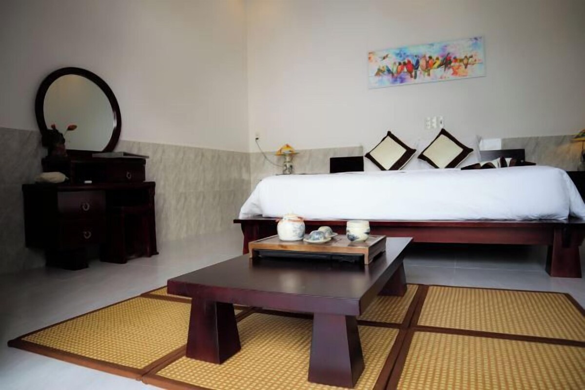 A hotel room with a bed, a dresser, a mirror, a painting on the wall, and a small table with decorative items.