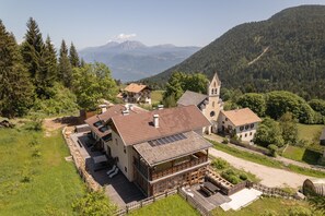 A traditional chalet with a wooden deck, a church, and a mountainous backdrop.