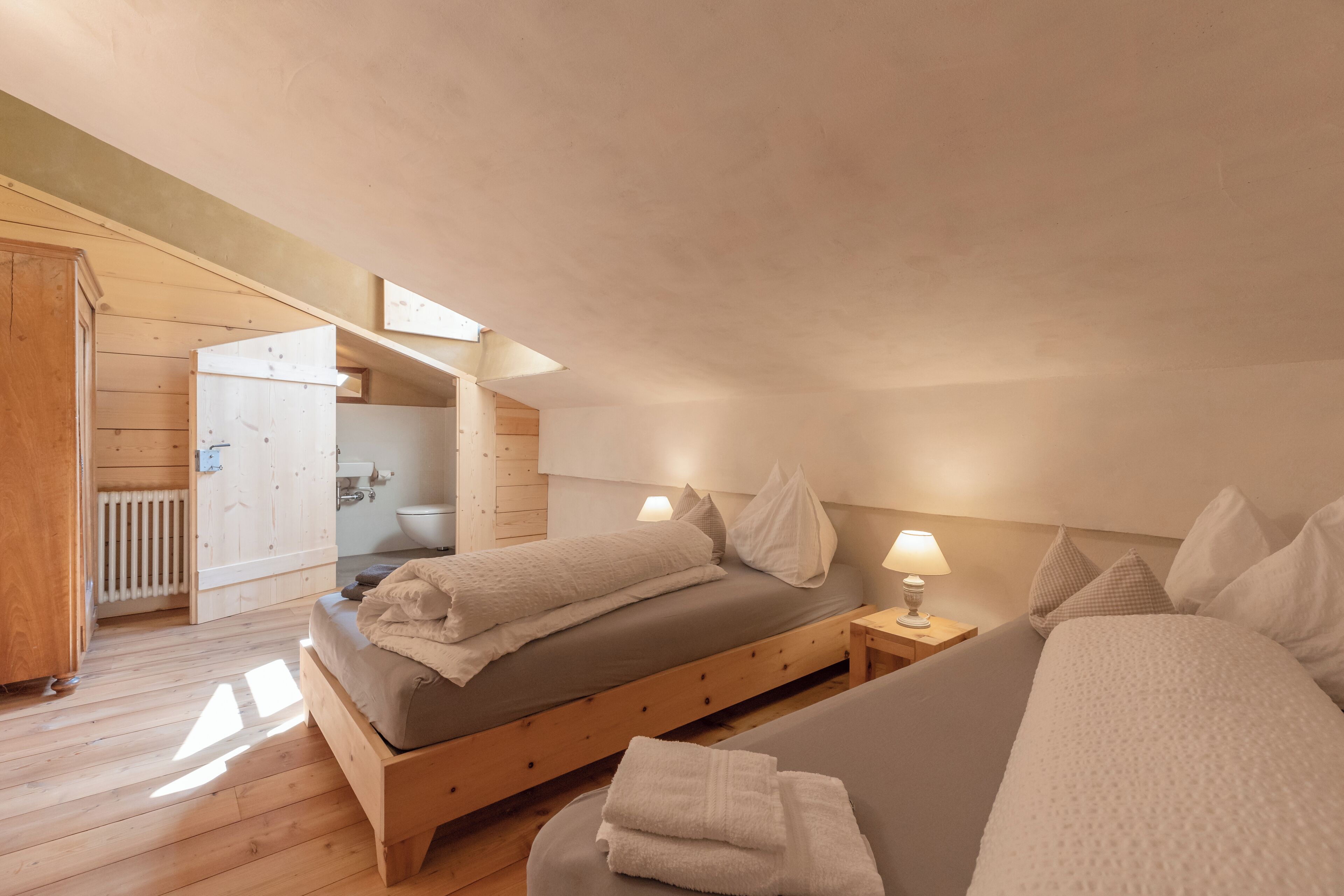 A bedroom with a wooden bed, a bedside table with a lamp, and a view of a bathroom.