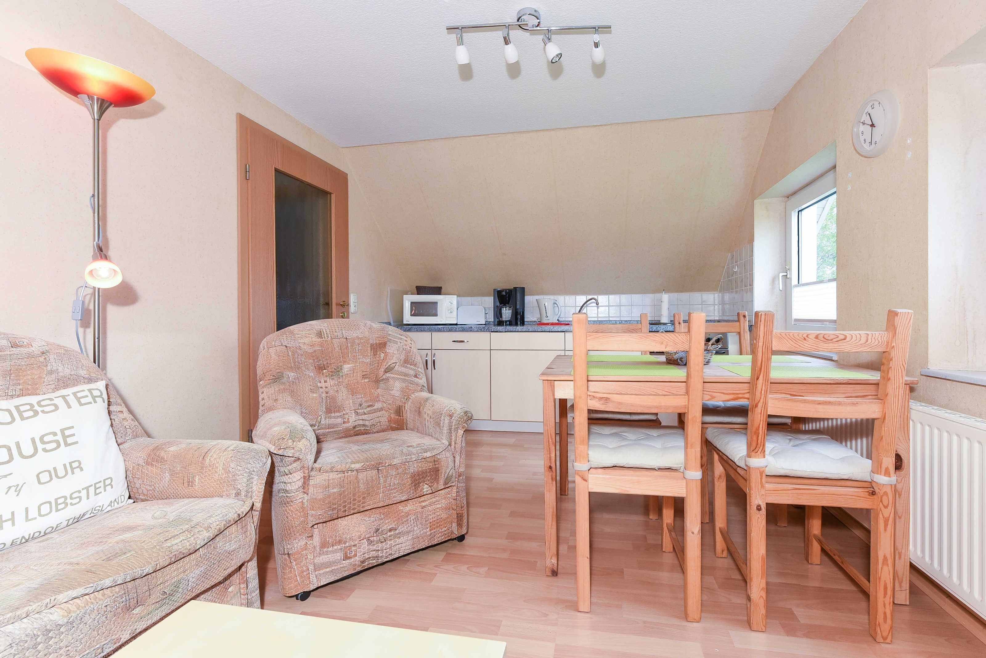 Un espacio habitable compacto con sofá, una mesa de comedor con sillas, una kitchenette y un ventanal.