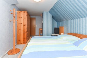A bedroom with a bed, wooden wardrobe, and a small table with a lamp.