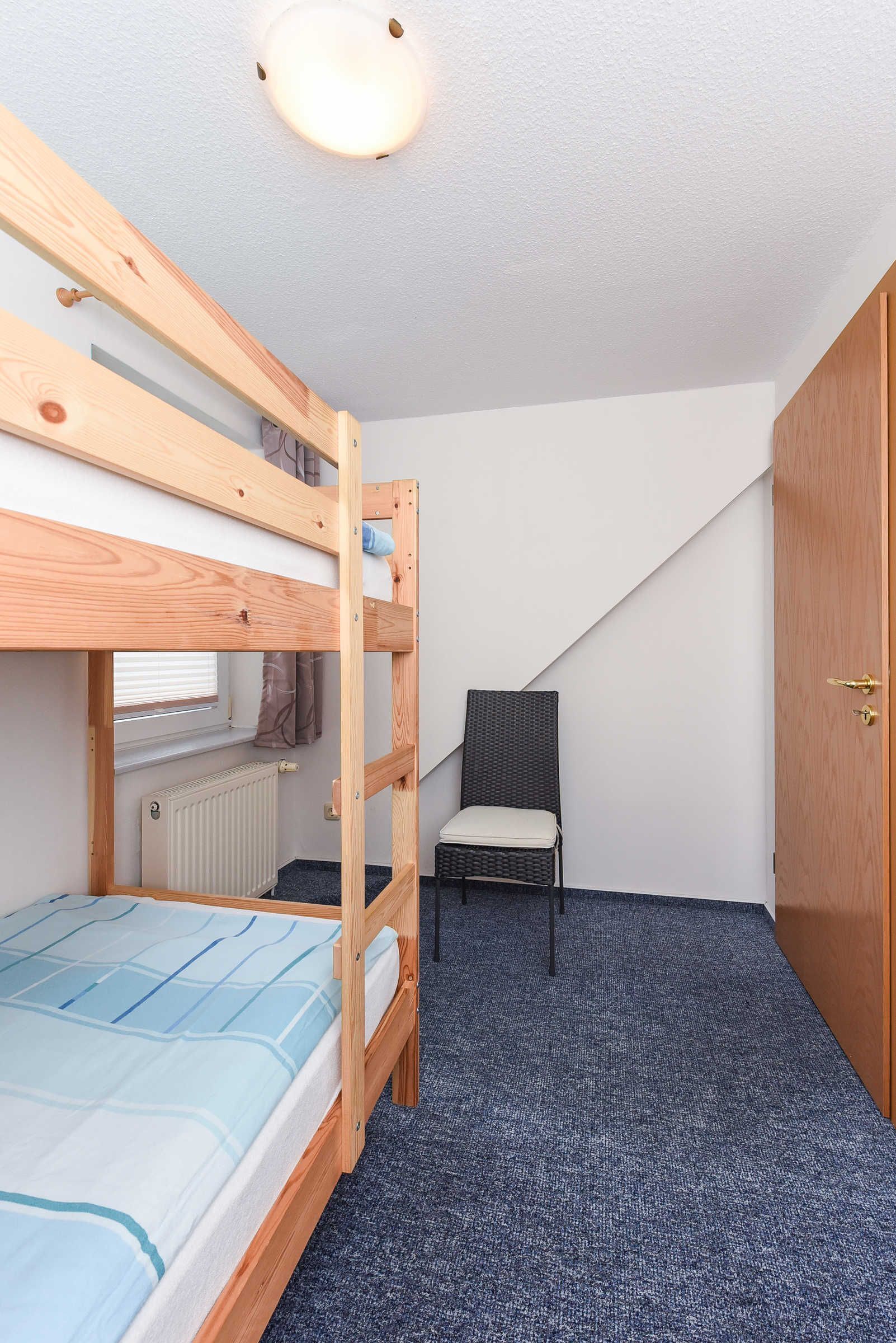 A bunk bed room with a window, a chair, and a door.