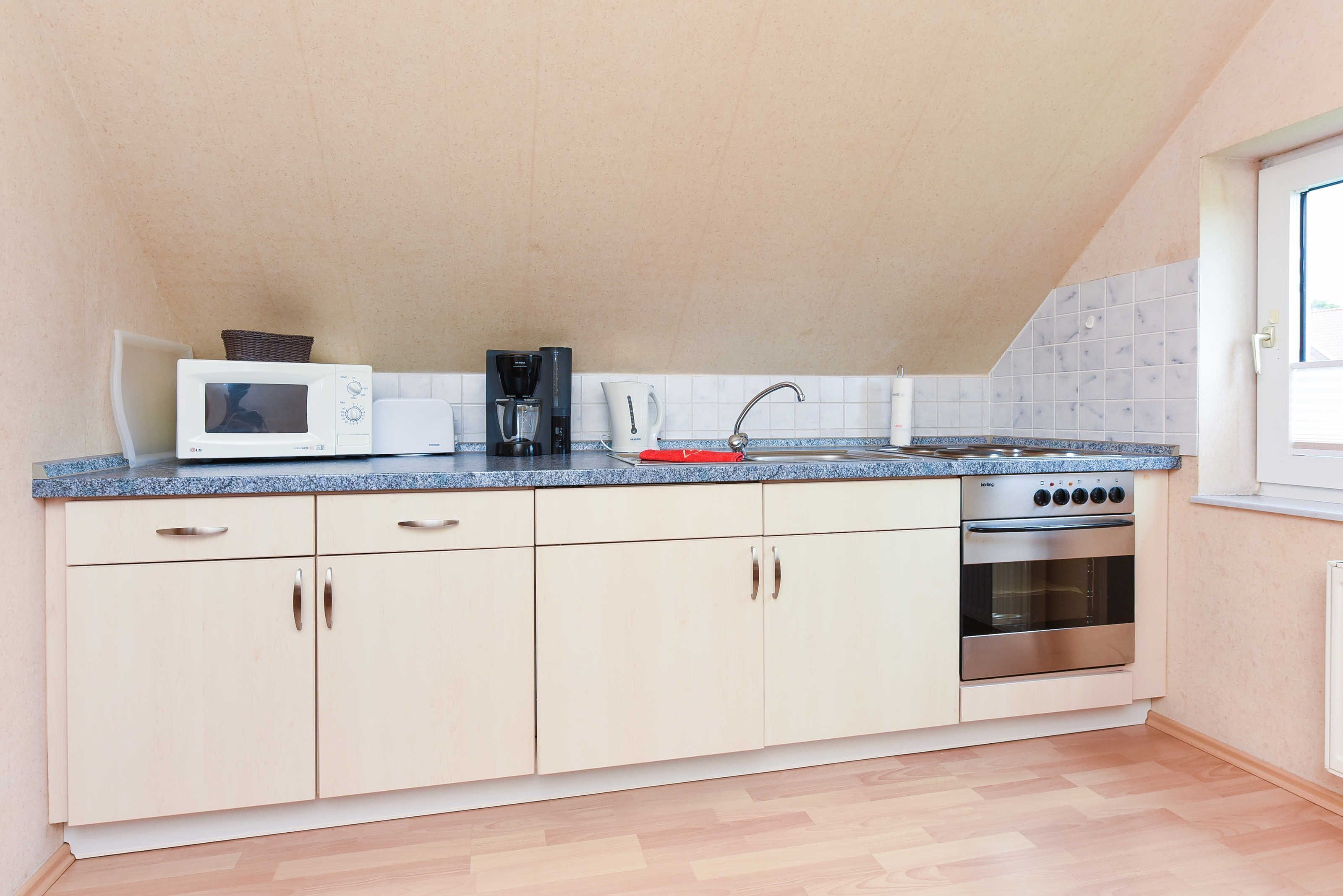 A compact kitchen with a microwave, coffee maker, kettle, and oven.